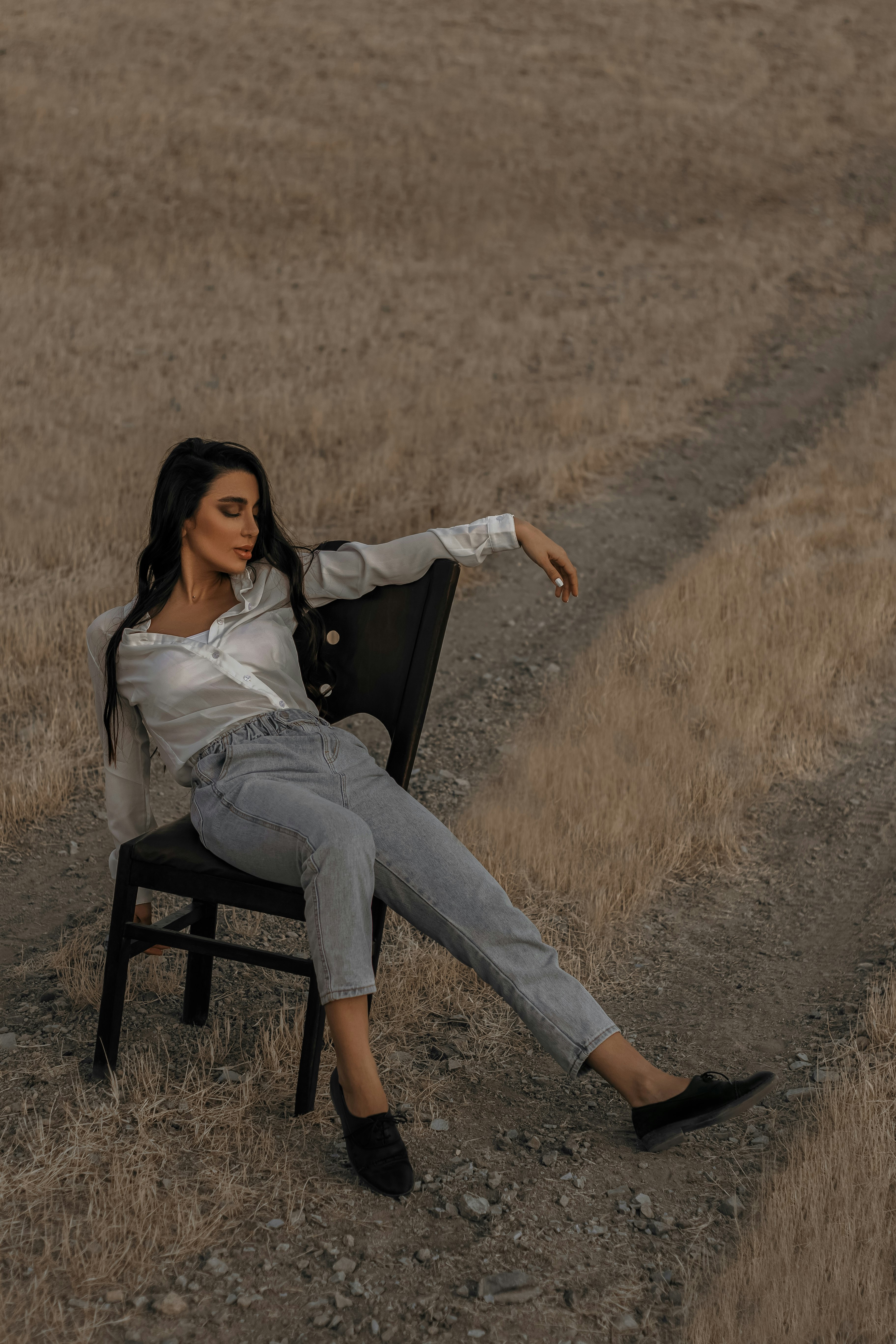 woman in white long sleeve shirt and blue denim jeans sitting on black wooden chair